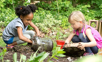 Two children playing with dirt and containers outdoors