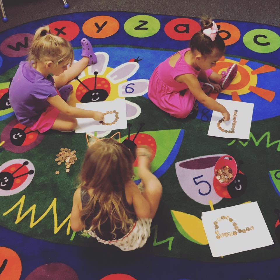Three children on a rug with letters, forming shapes with small objects