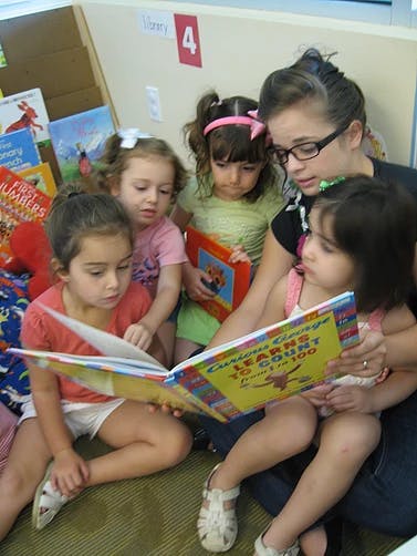 Adult person reading a book to four children