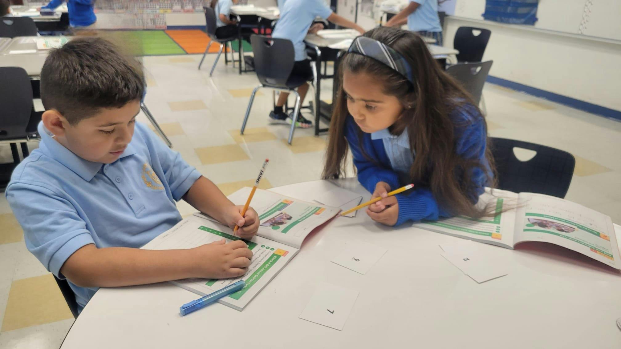Two children in uniform working on schoolwork at a desk in a classroom