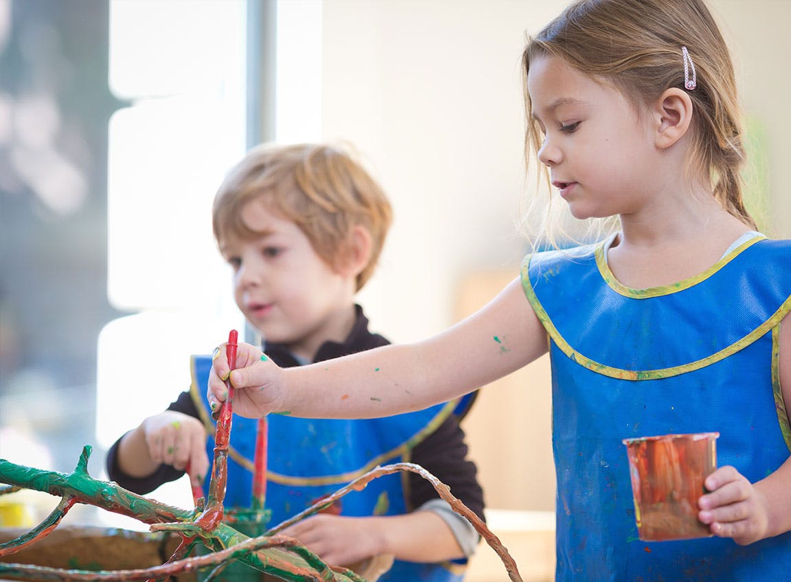 Two children in blue smocks painting branches