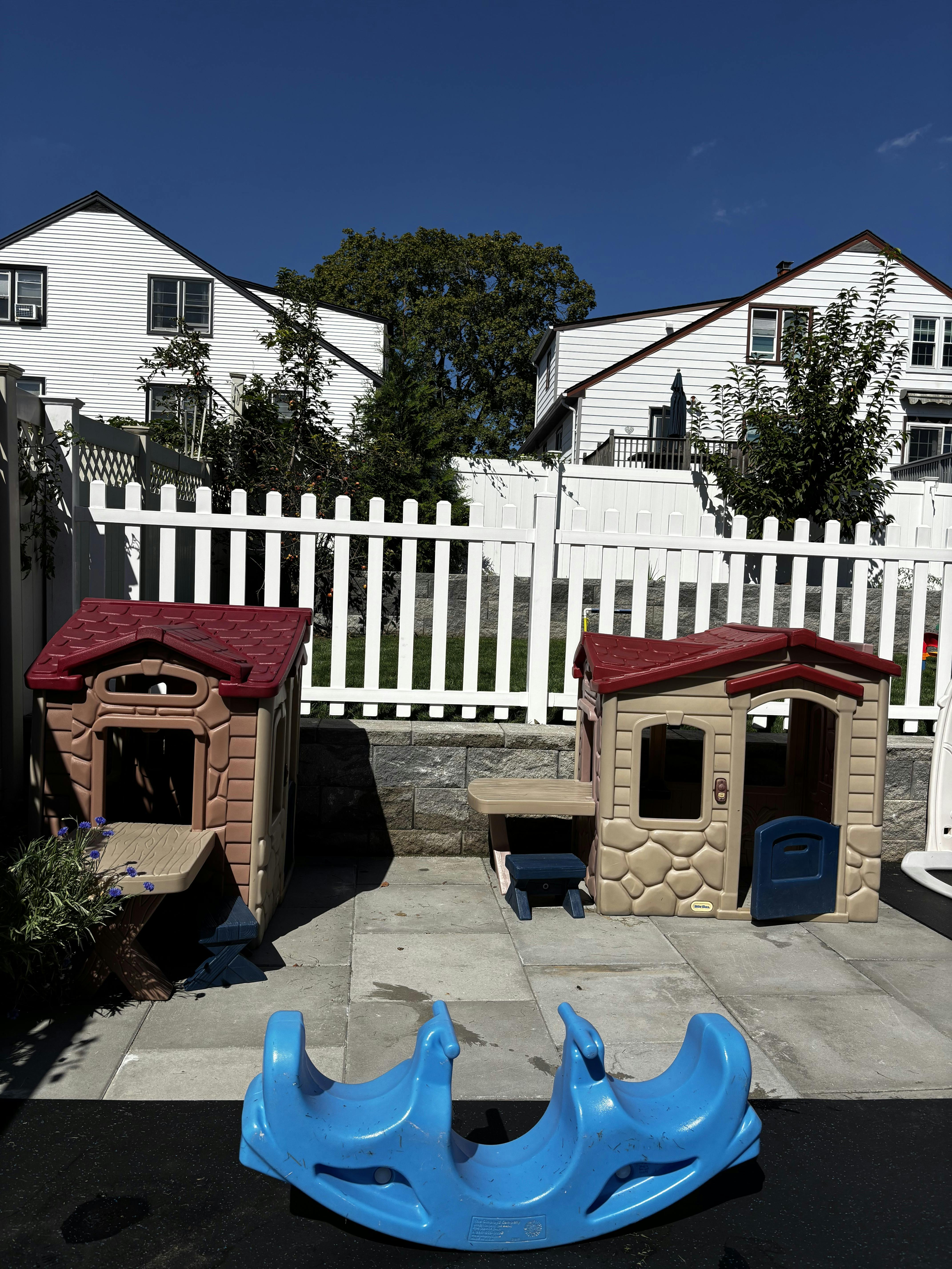 Two playhouses and a blue seesaw on a patio