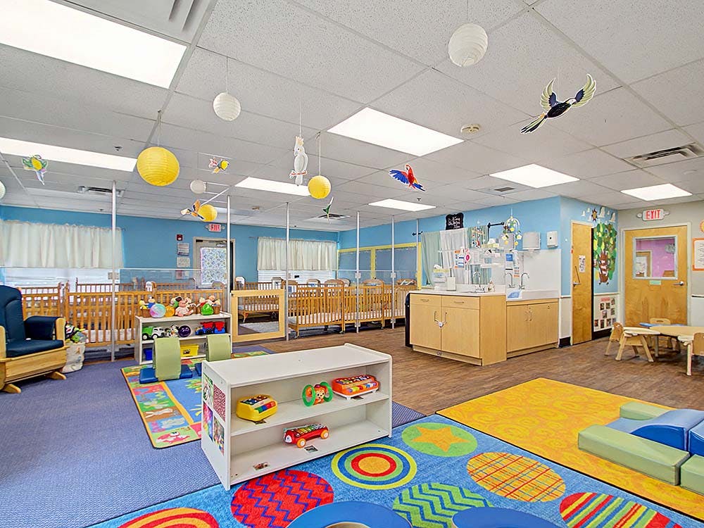 Baby room with multiple cribs, a changing station, and colorful play rugs