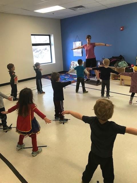 Adult and children doing an exercise with arms outstretched in a room