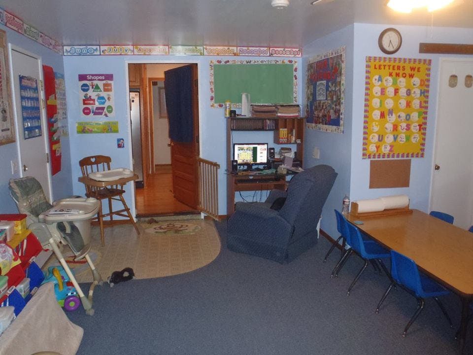 Classroom with a high chair, computer desk, and table with blue chairs