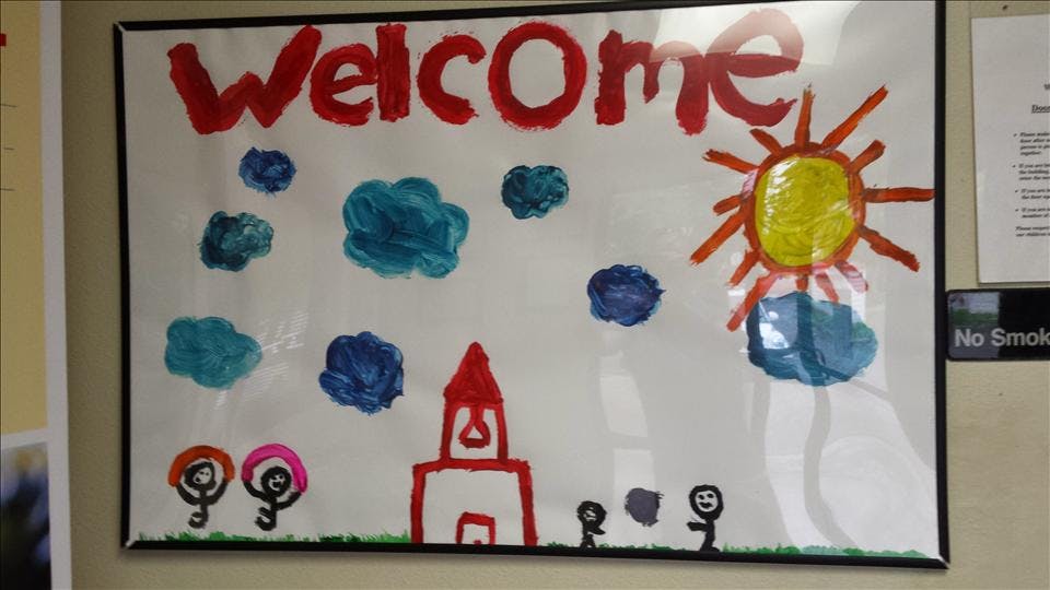 Child's drawing with "Welcome" text, sun, clouds, people, and a building