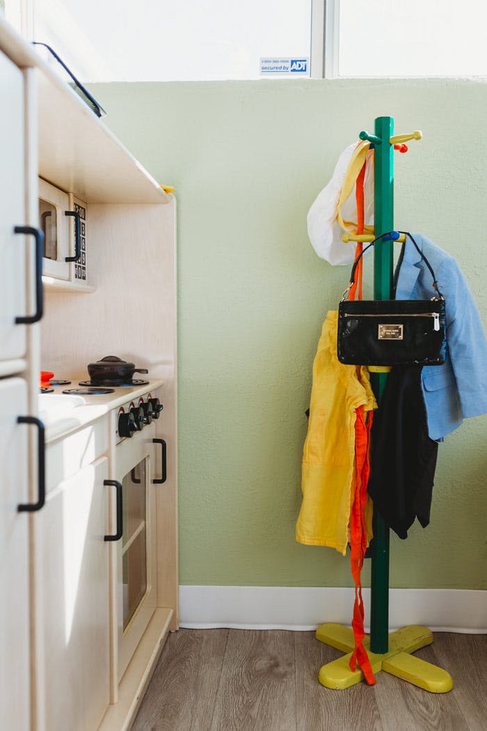 Play kitchen next to a coat rack with clothes and a purse