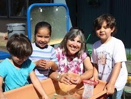 Adult and three children playing with water in a bin