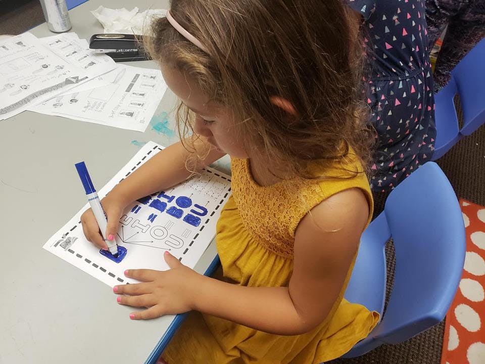 Child coloring a worksheet with a blue marker