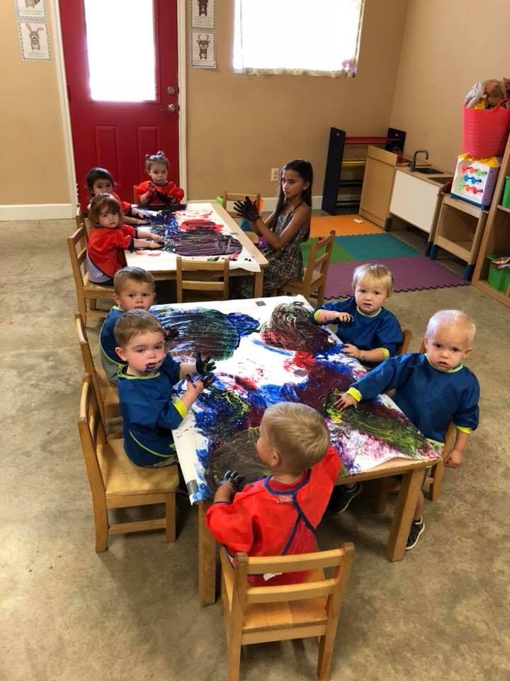 Children finger painting at tables in a classroom