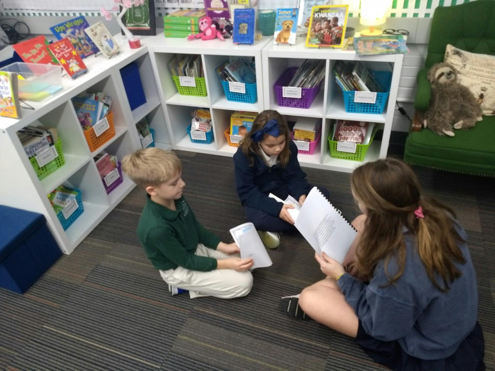 Three children sitting on the floor reading papers