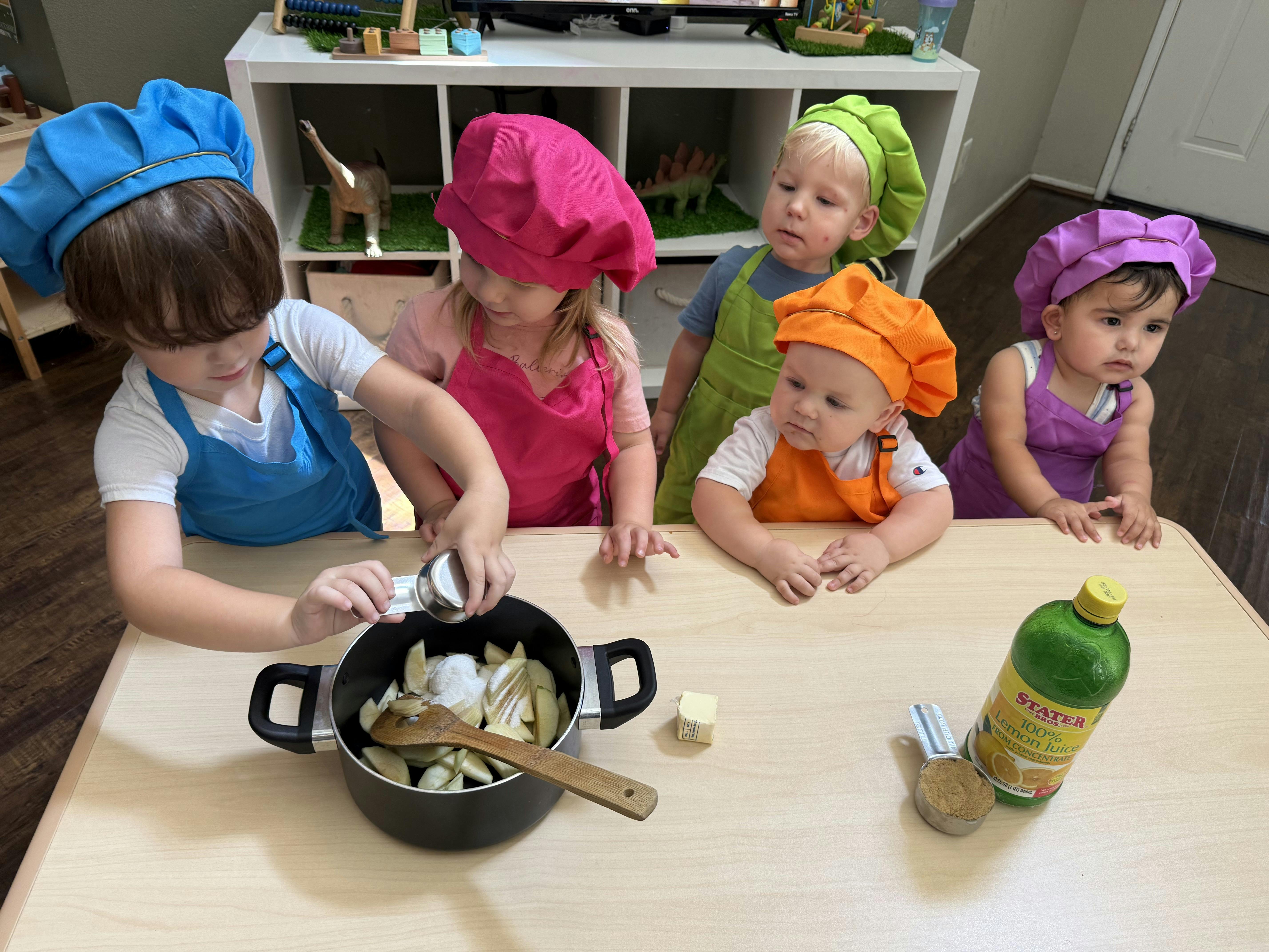 Group of children wearing chef hats and aprons cooking with sliced fruit