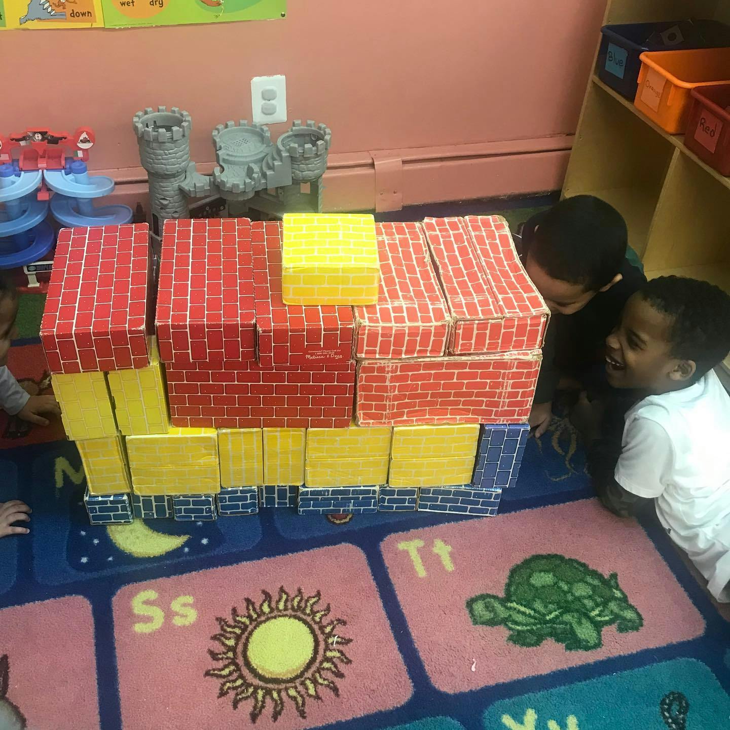 Two children playing with large building blocks on a rug