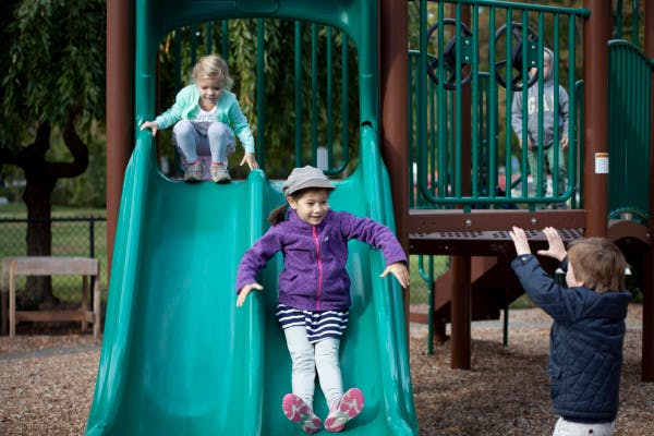 Children playing on a green slide at a playground