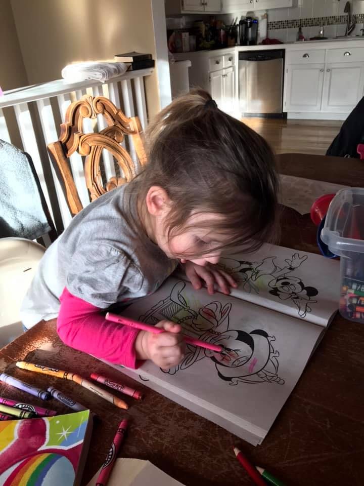 Child coloring in a coloring book with a pink crayon