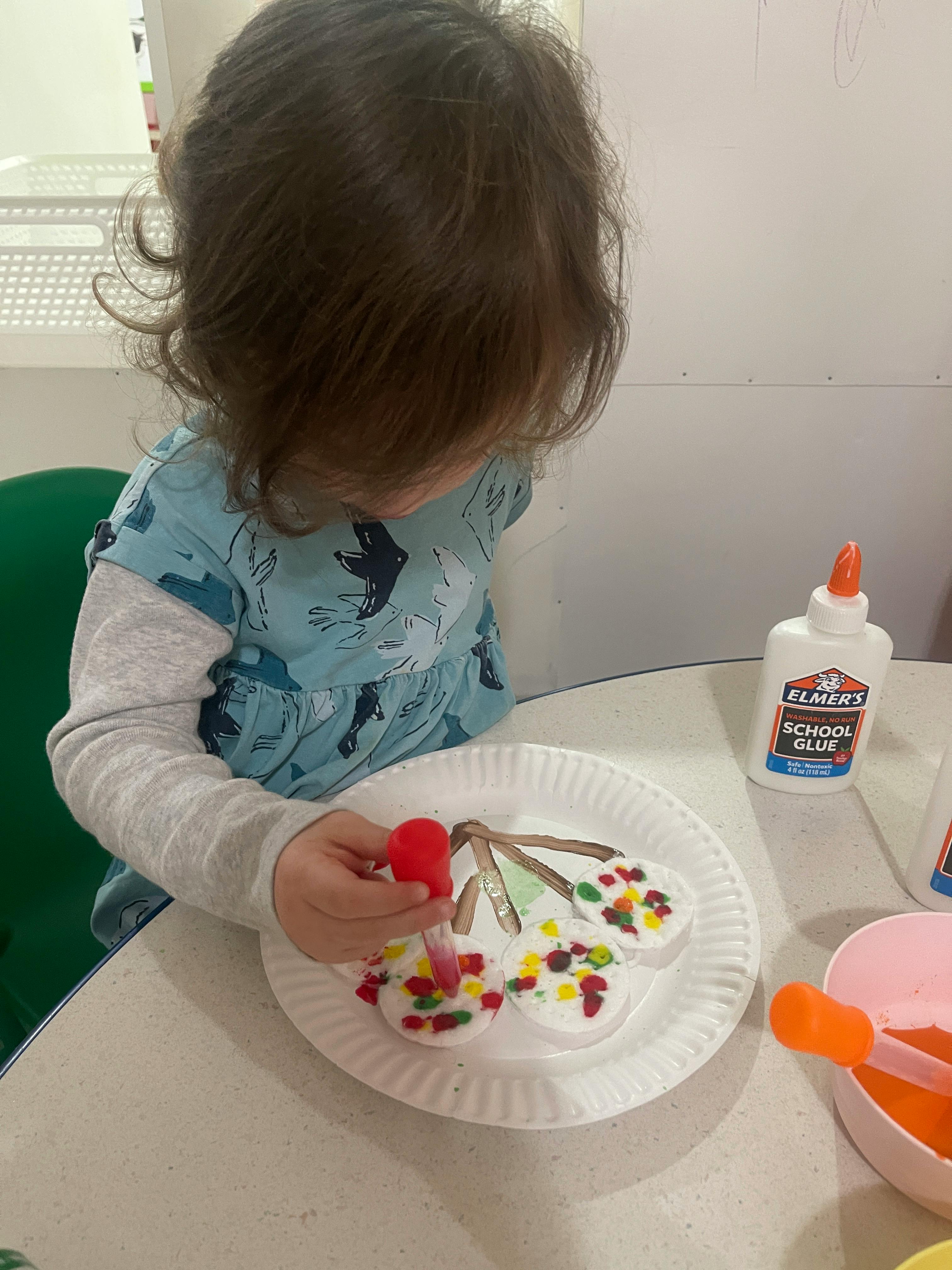 Child decorating a craft with colorful sprinkles and glue