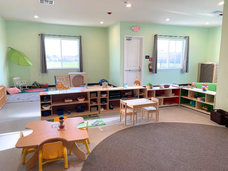 Classroom with small tables and chairs, shelves with toys and books
