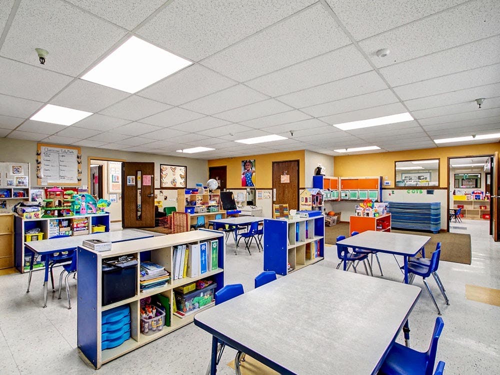 Classroom with small tables and chairs, shelves, and play areas