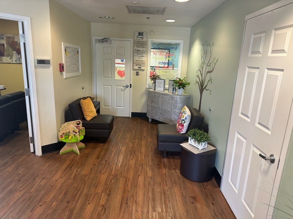 Waiting area with two dark armchairs, a console table, and a tree decal on the wall