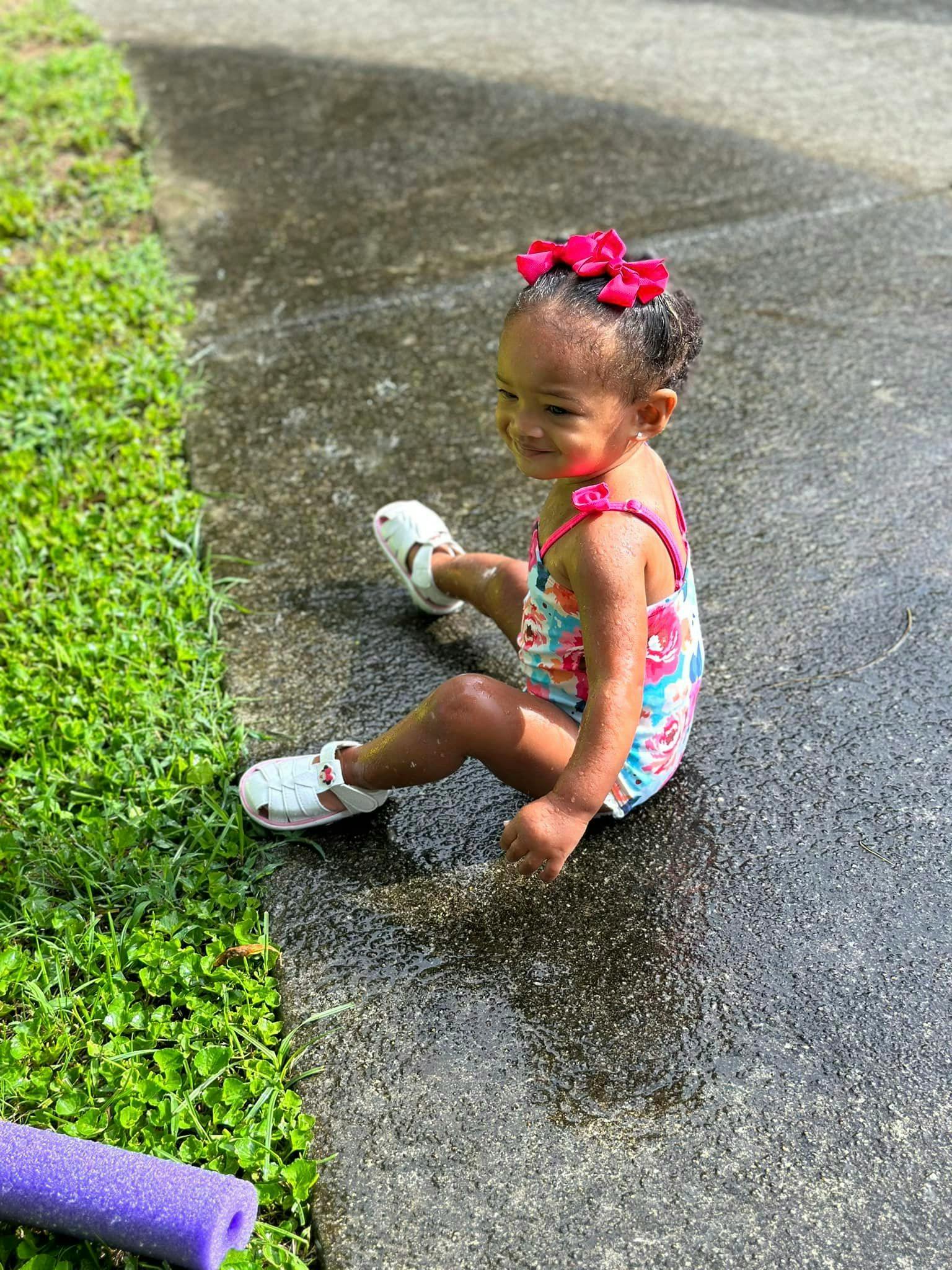 Child sitting on wet pavement next to grass