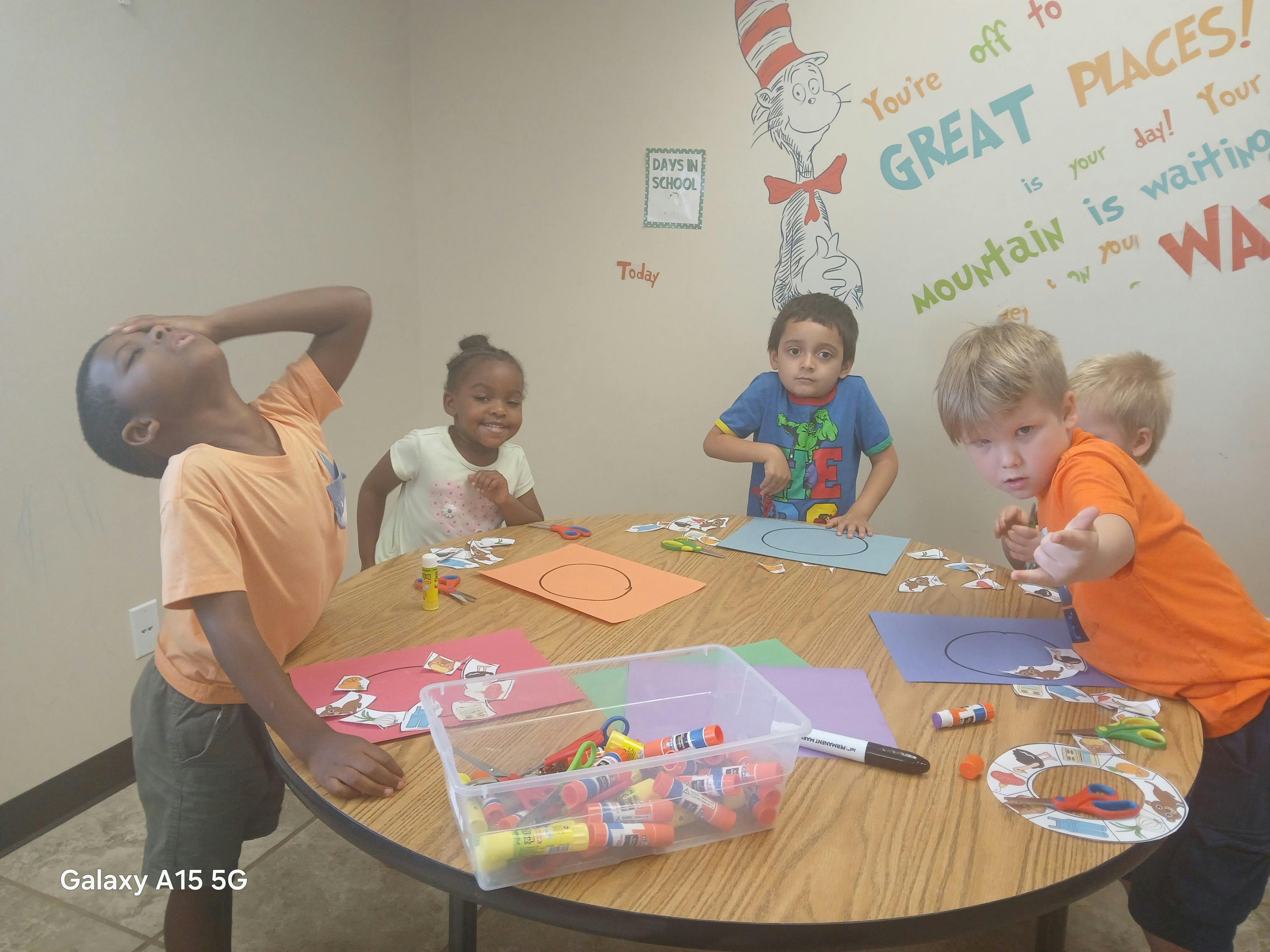 Four children doing a craft project at a round table in a classroom