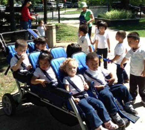 Children in a multi-seat stroller with other children and adults nearby