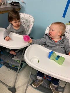 Two children in high chairs, one holding a pink cup