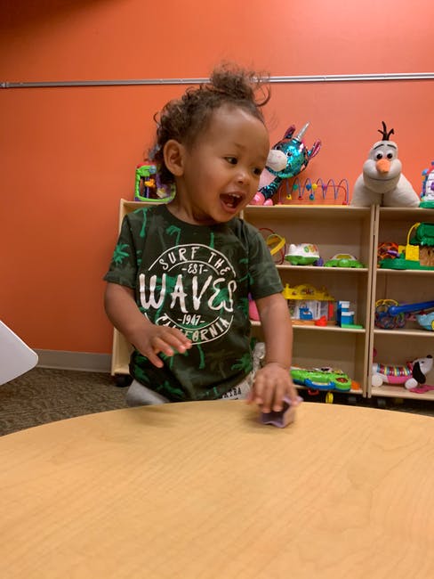 Child standing at a table, playing with a small object