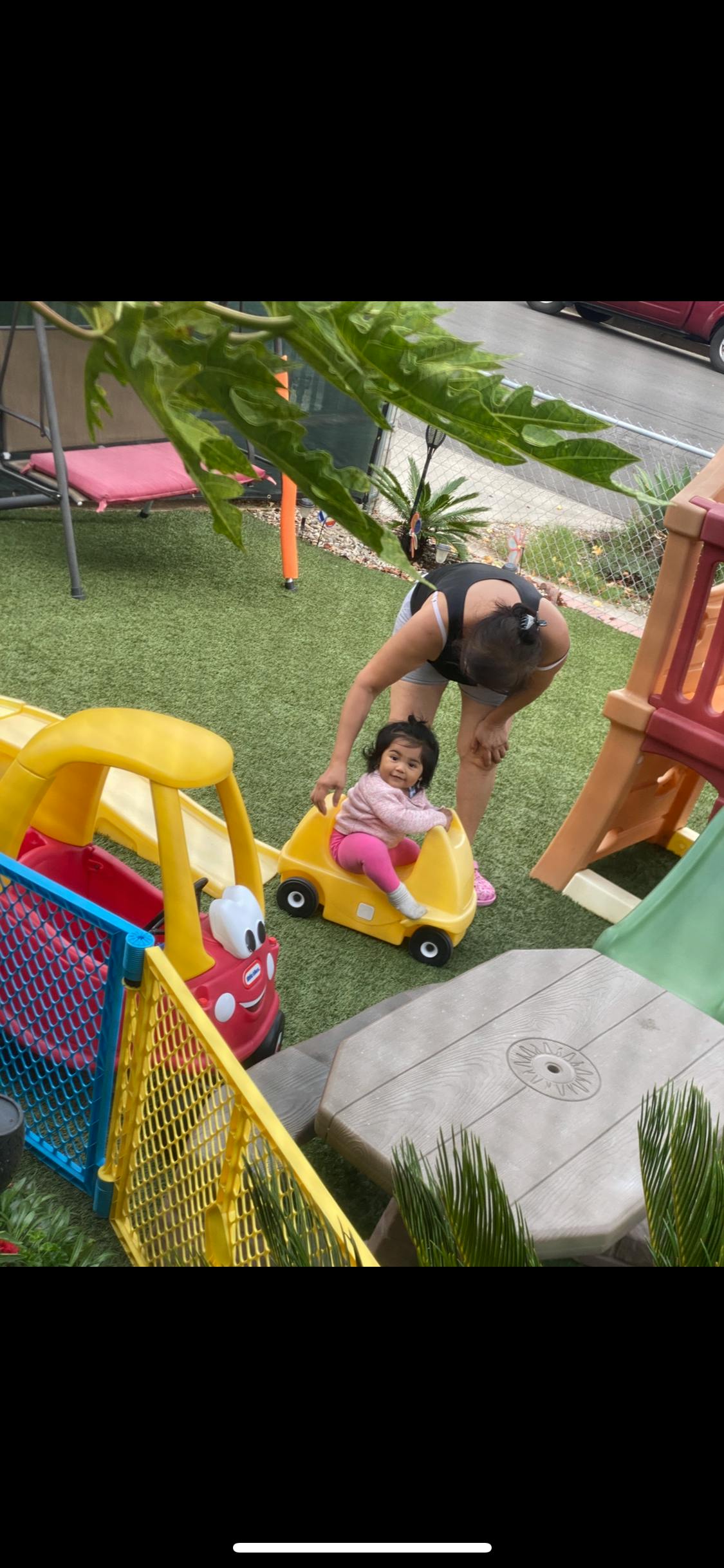 Person pushing a child in a yellow toy car on artificial grass