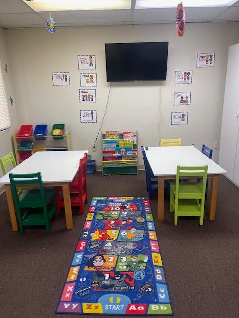Classroom with small tables and chairs, a TV, and a colorful rug