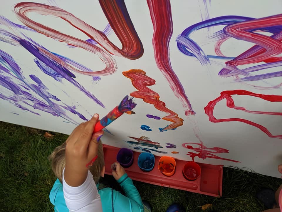 Child painting on a large white surface with a brush and paint pots