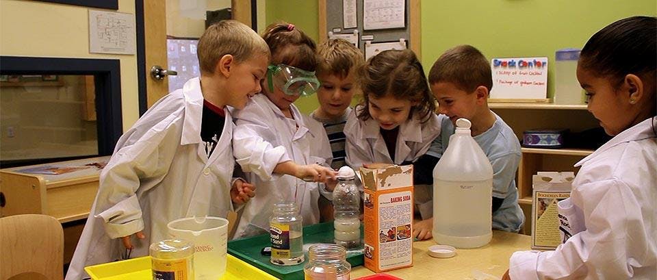 Children in lab coats doing a science experiment in a classroom