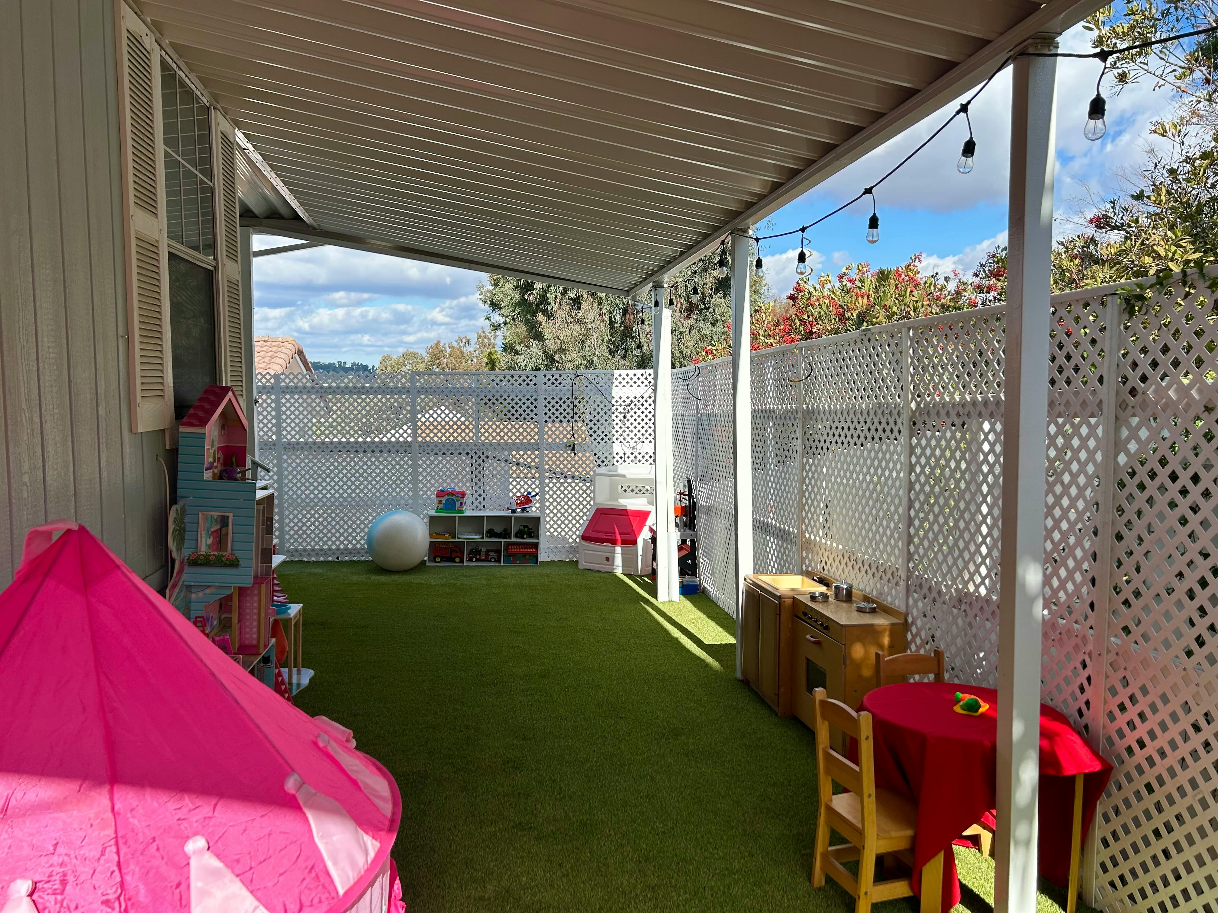 Outdoor play area with artificial turf, a pink tent, and small tables