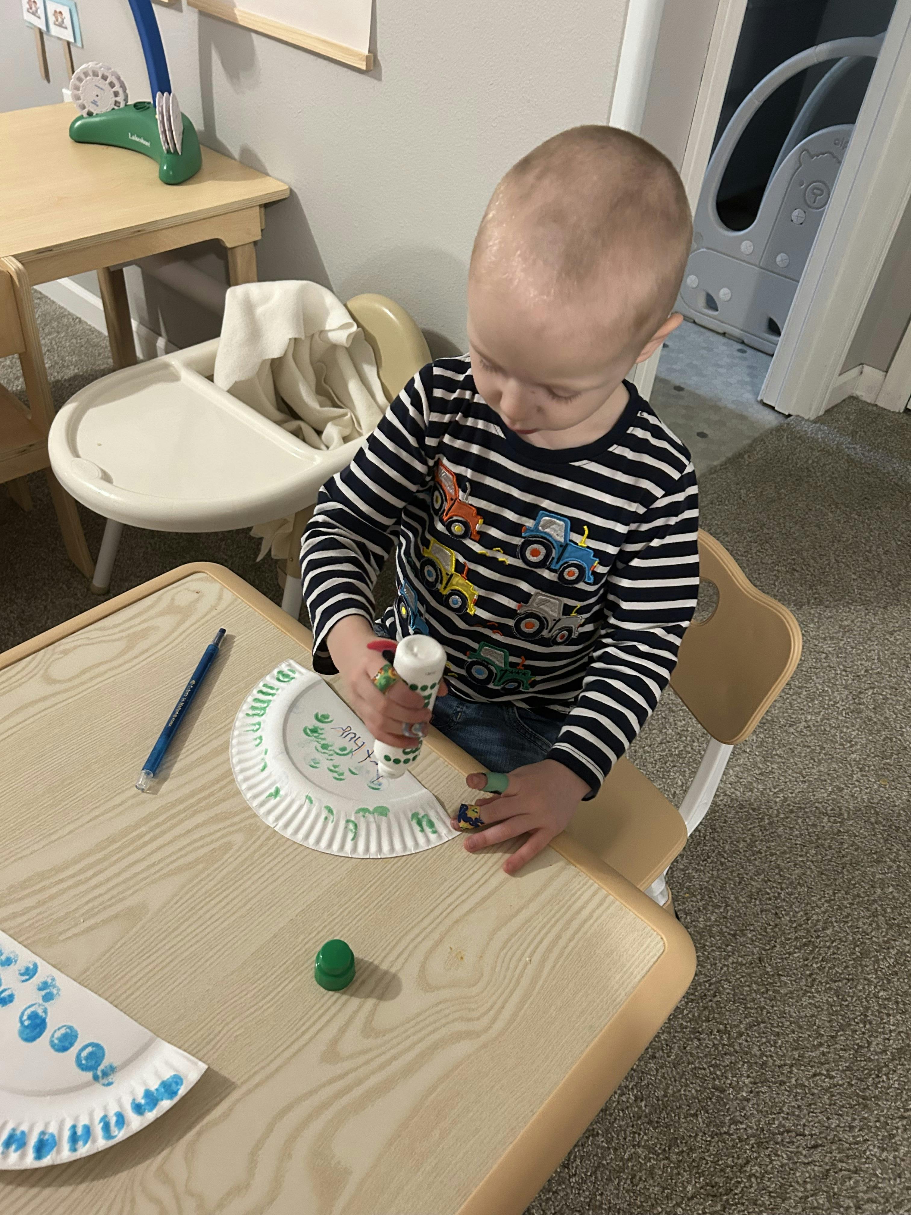 Child sitting at a small table using a glue bottle on a paper plate