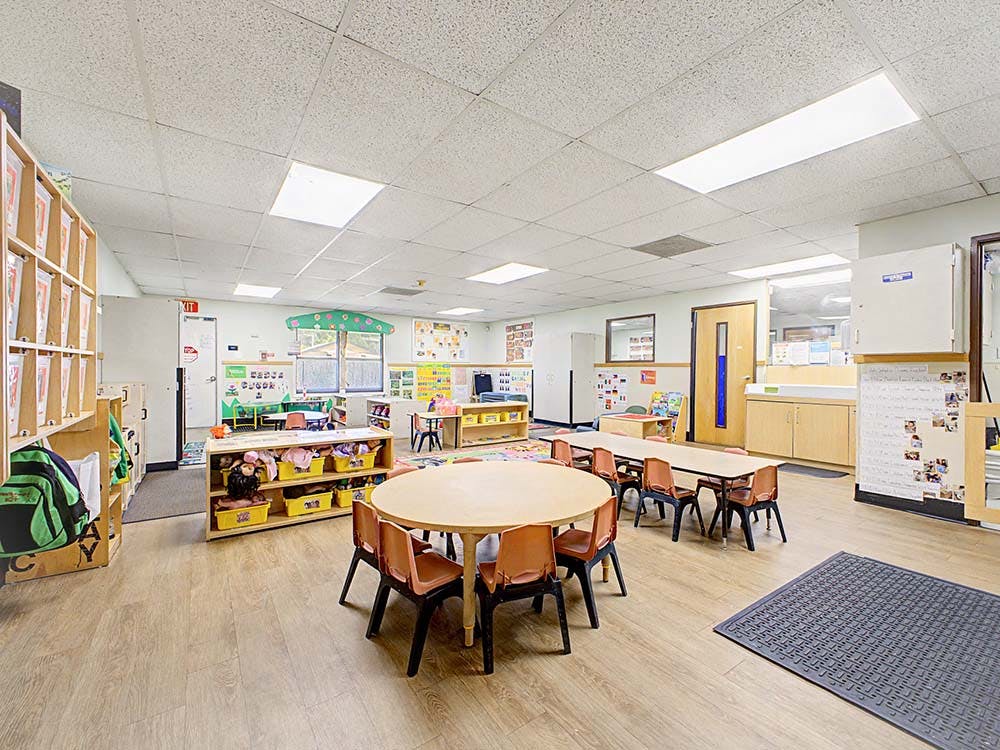 Empty classroom with small tables and chairs, shelves, and learning materials