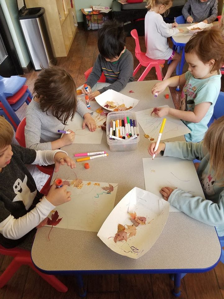 Children at a table doing crafts with markers and leaves