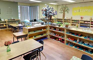 Classroom with tables, chairs, and shelves with learning materials