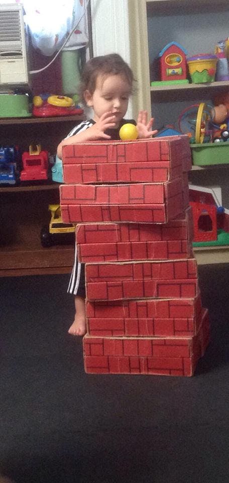 Child playing with a stack of red brick-patterned boxes