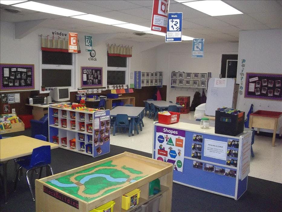 Classroom with small tables and chairs, shelves of toys, and educational posters