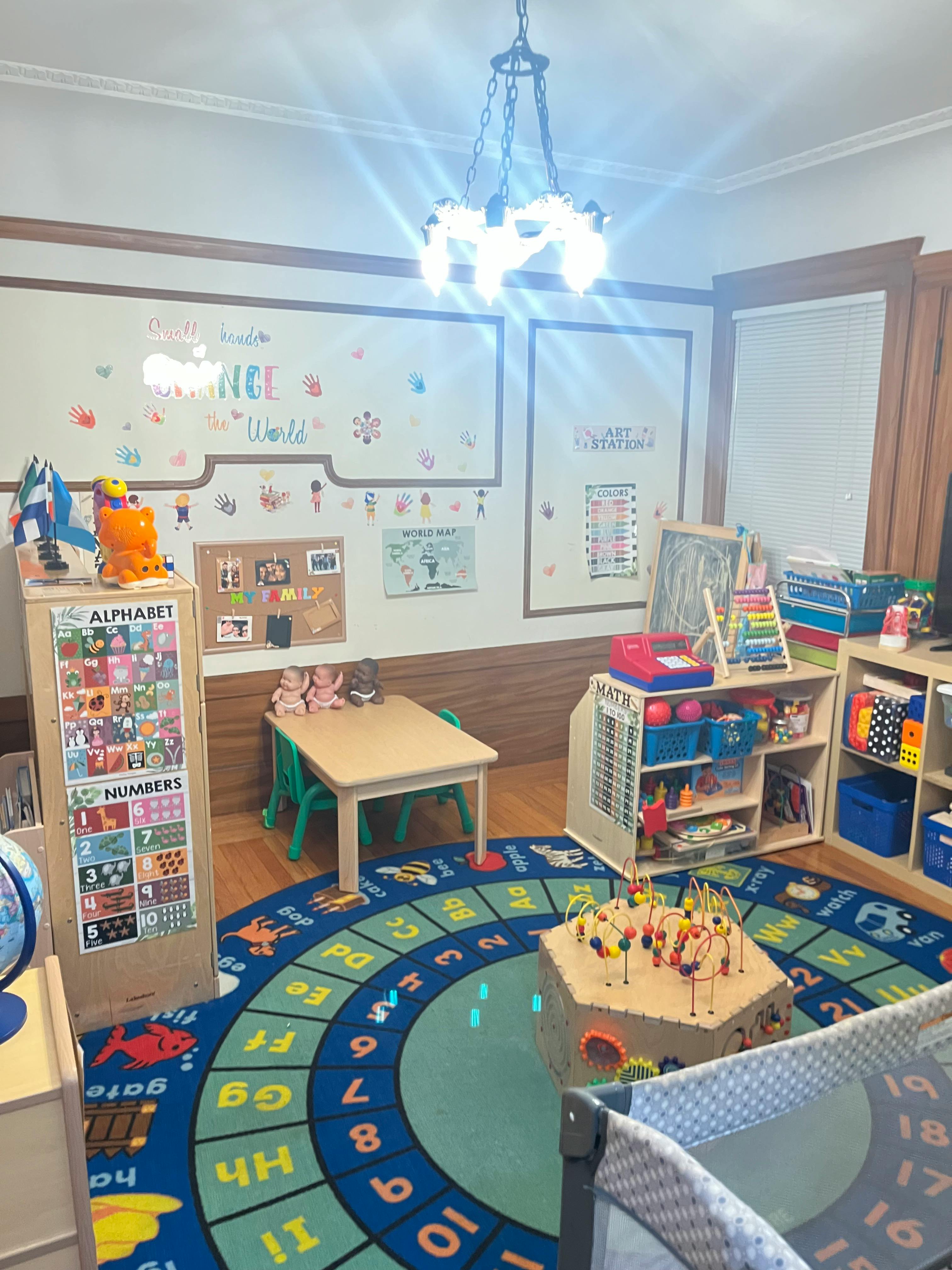 A classroom with a colorful alphabet rug, small tables, and shelves with toys