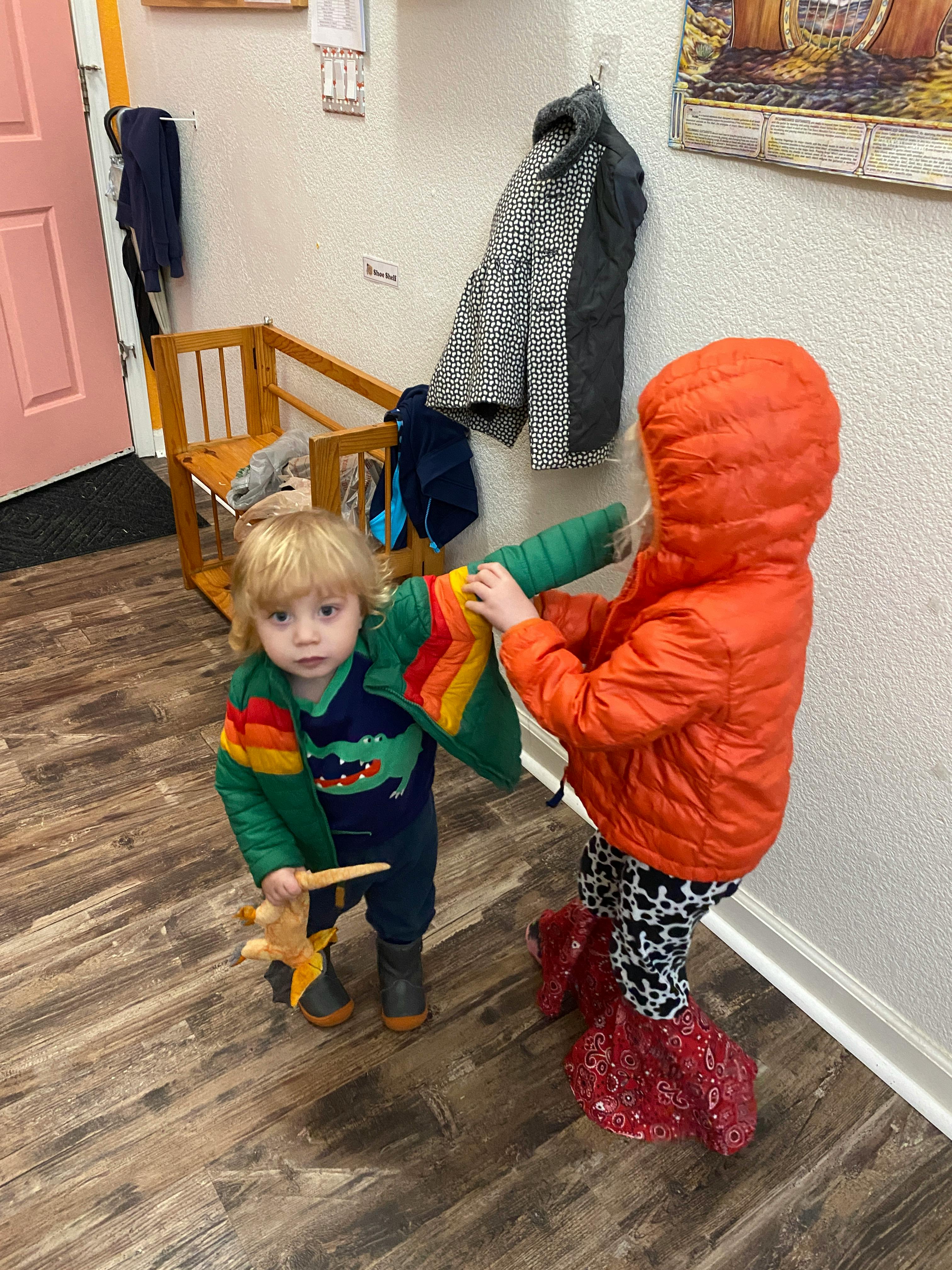 Child helping another child put on a jacket