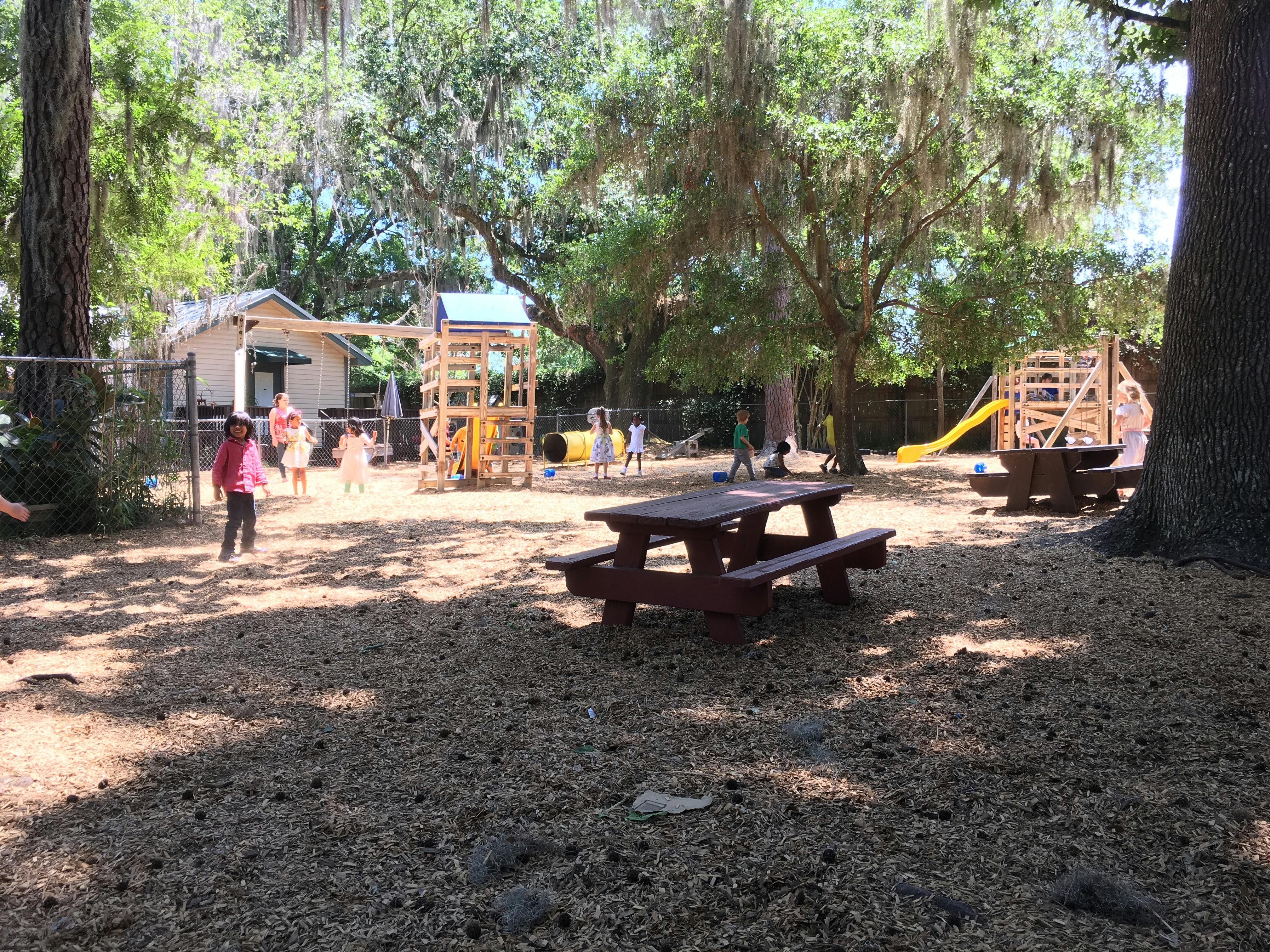 Children playing on a playground with wooden structures and picnic tables