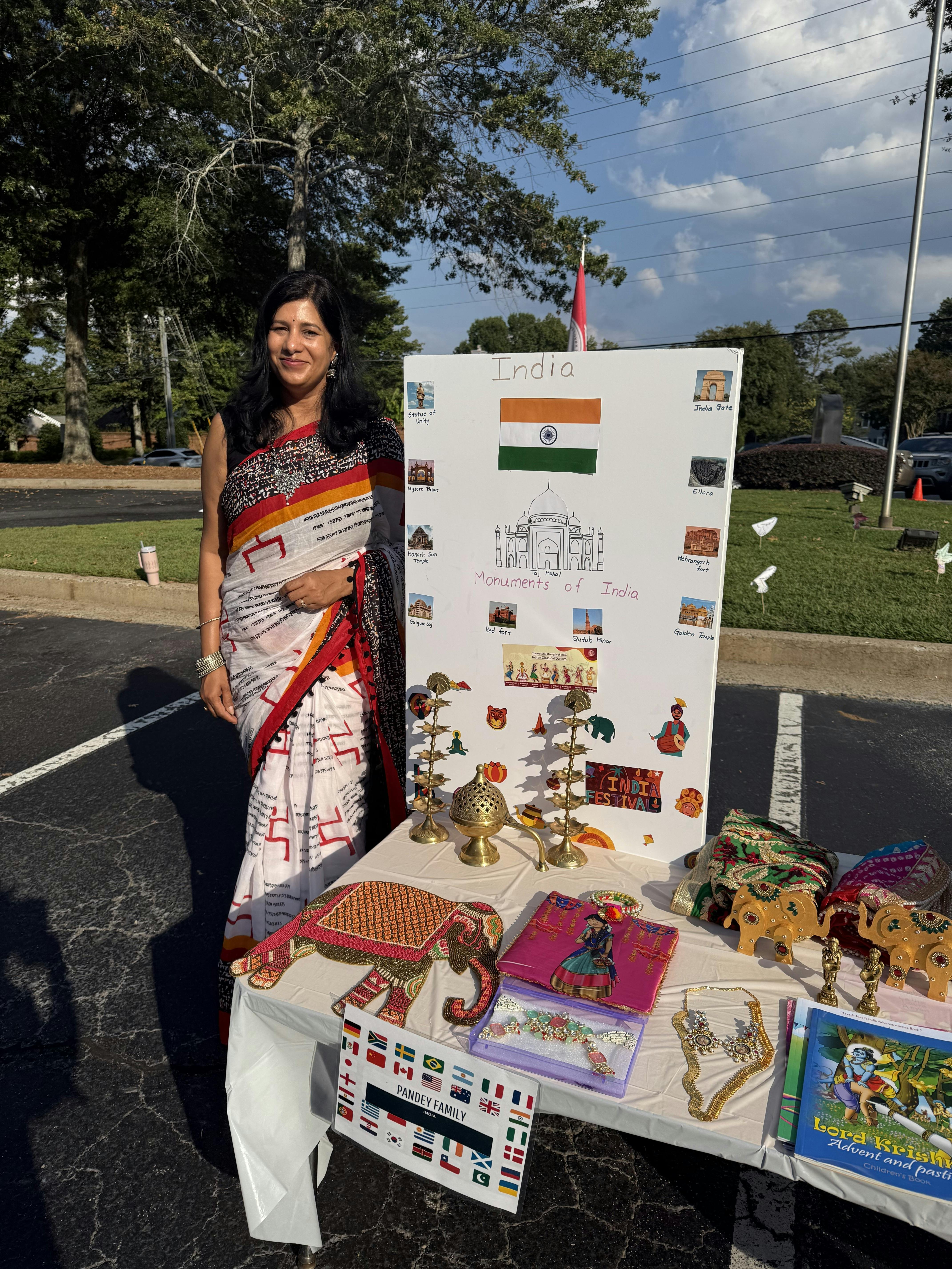 Person in a sari standing next to a display board and table with cultural items