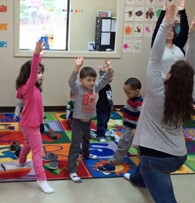 Adults and children raising their arms in a classroom