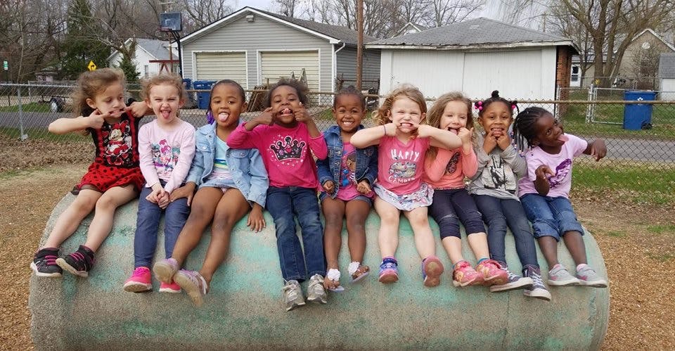 Group of children sitting on a large pipe, some making faces