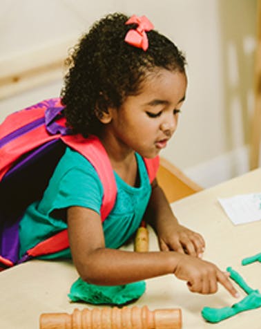 Child playing with green modeling clay at a table
