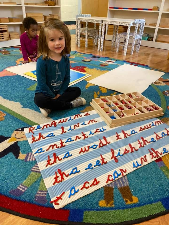 Child sitting on a rug with a letter mat and another child in the background