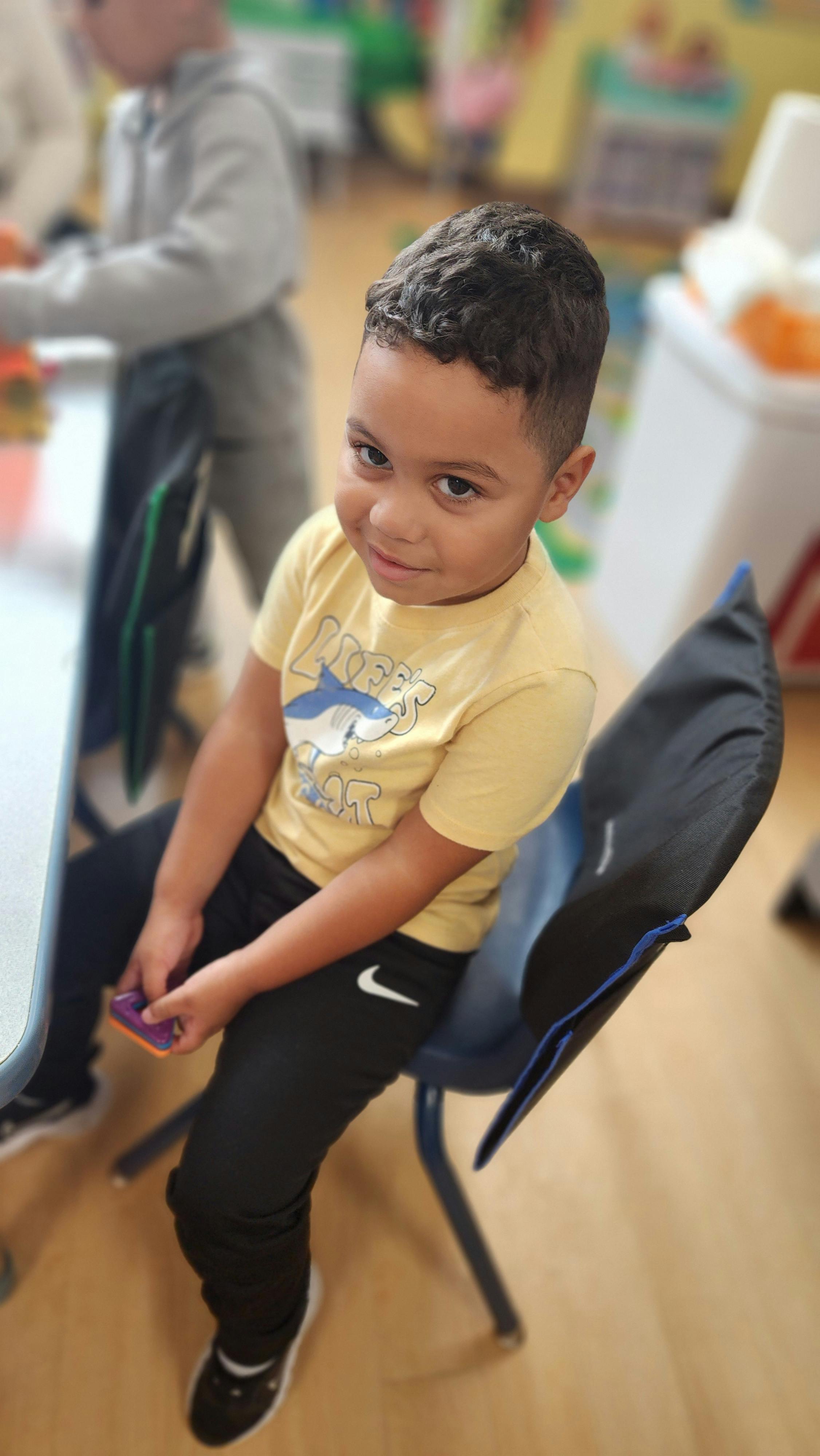 Child sitting on a chair in a classroom, holding a small object