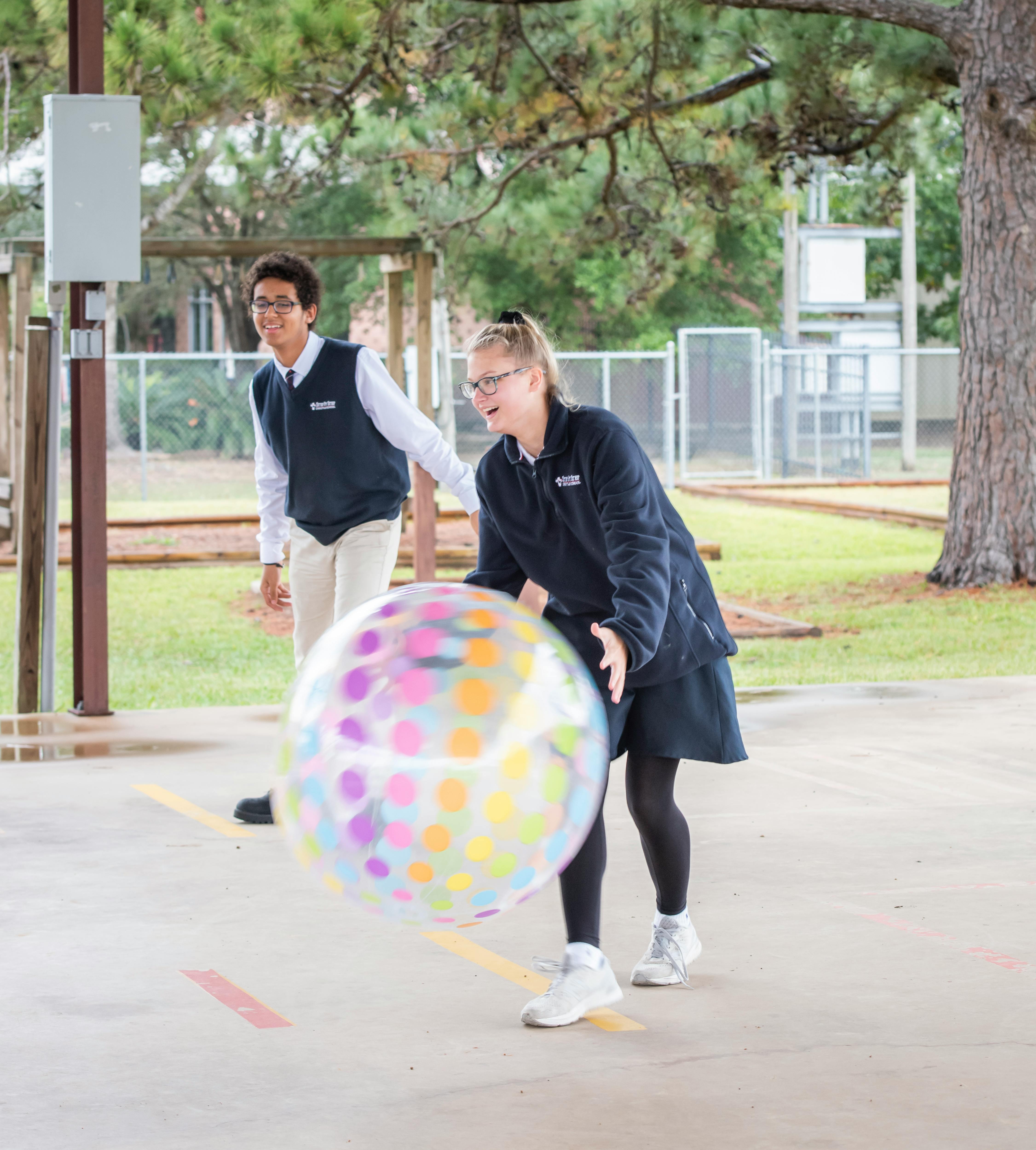 Two teens in school uniforms playing with a large polka-dot inflatable ball