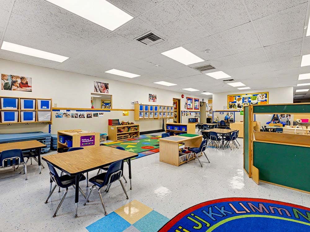Empty colorful classroom with small tables, chairs, and learning materials